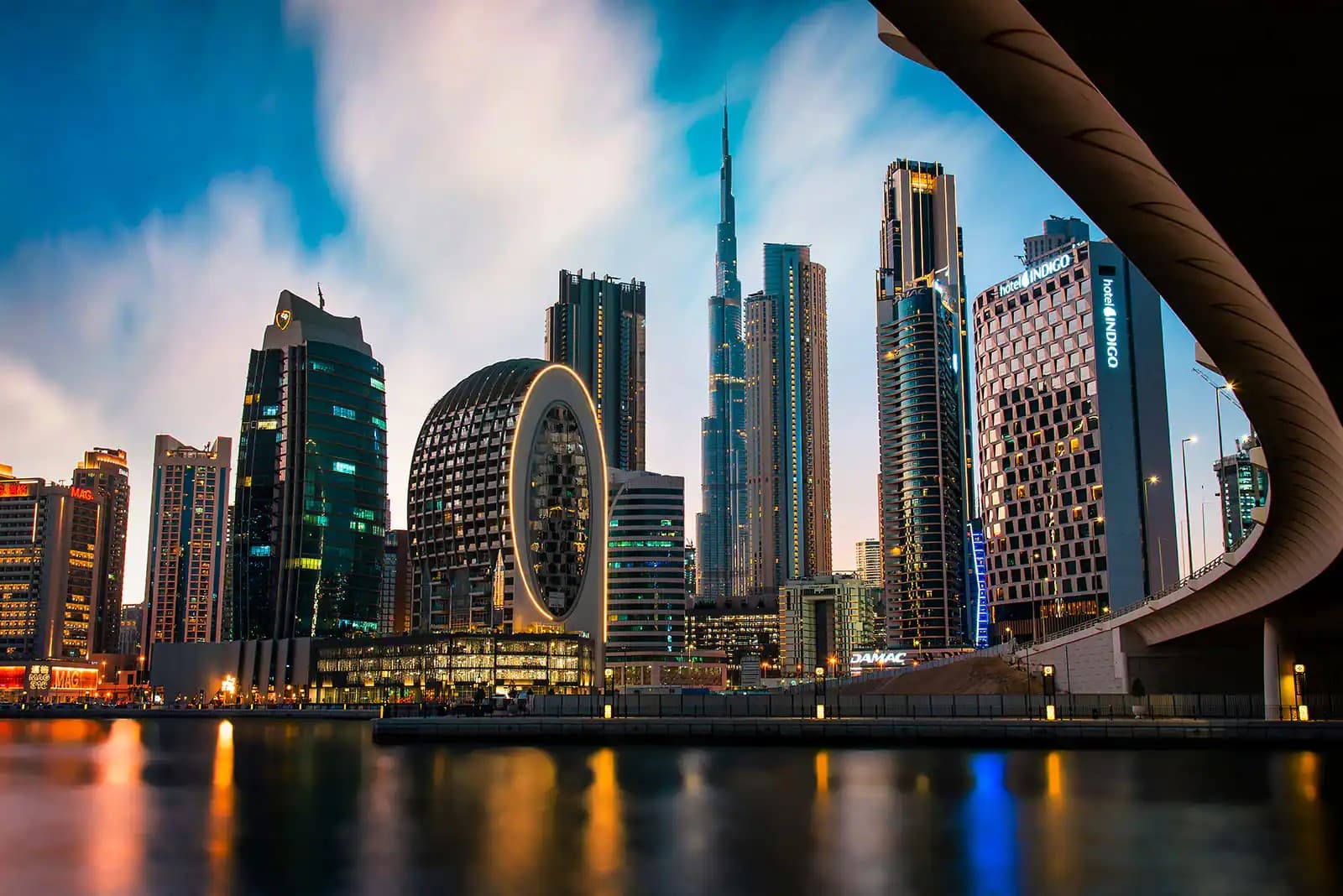 Business Bay towers and the Opus along the Dubai Water Canal at dusk with Burj Khalifa behind